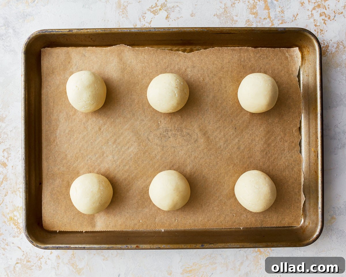 Shaped balls of pandebono bread dough neatly arranged on a parchment-lined baking sheet, spaced apart for baking.