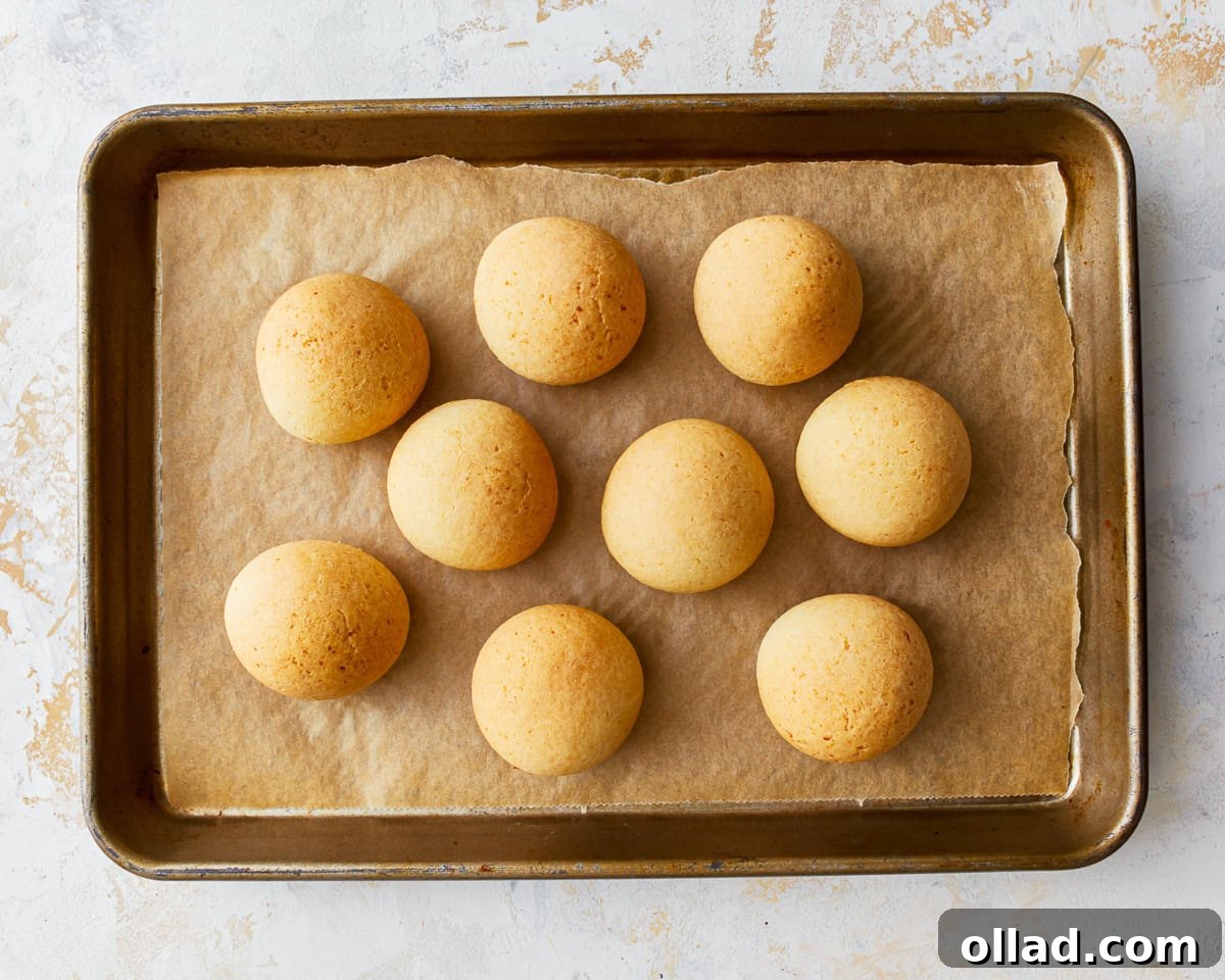 Freshly baked pandebono, golden brown and puffed up, cooling on a parchment-lined baking sheet after coming out of the oven.