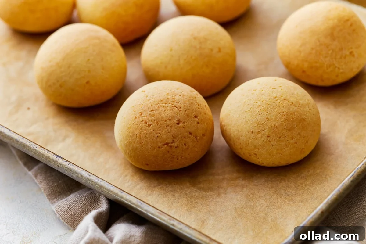 Side view of freshly baked Pandebono, Colombian cheese bread, on a parchment-lined baking sheet, showcasing its golden crust and round shape.