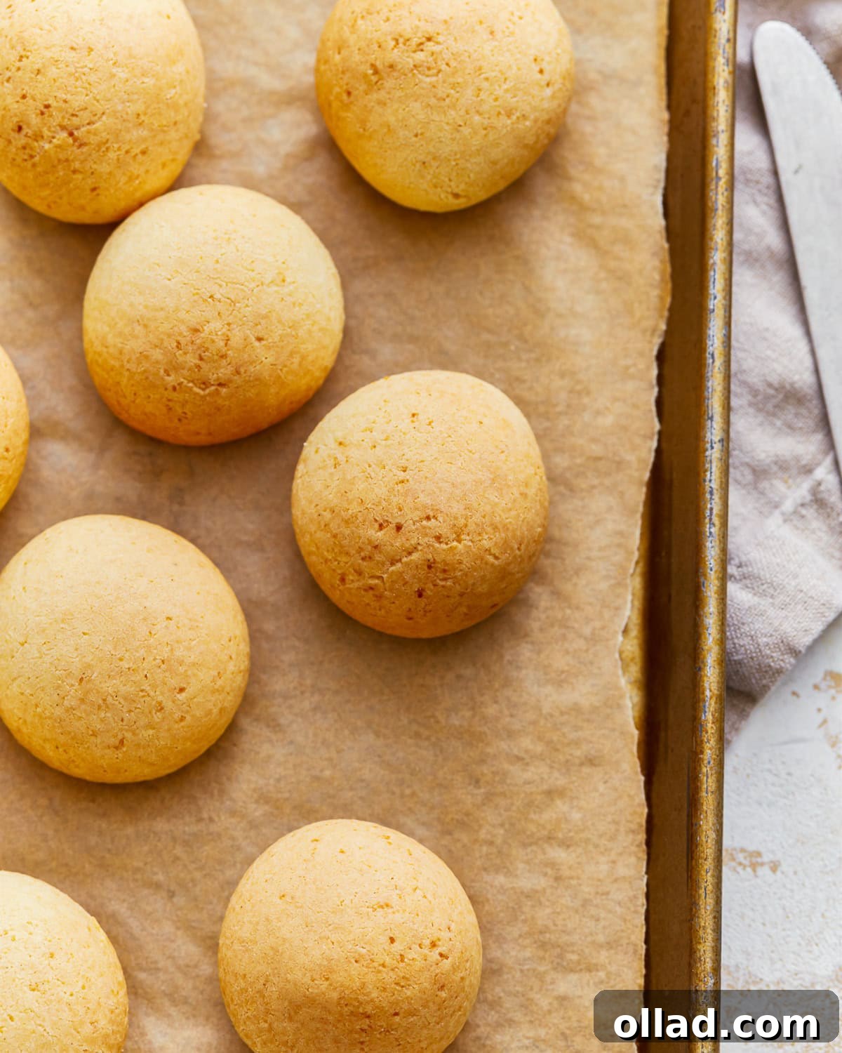 Overhead view of several Pandebono, Colombian cheese bread, on a parchment-lined baking sheet, showing their golden tops.
