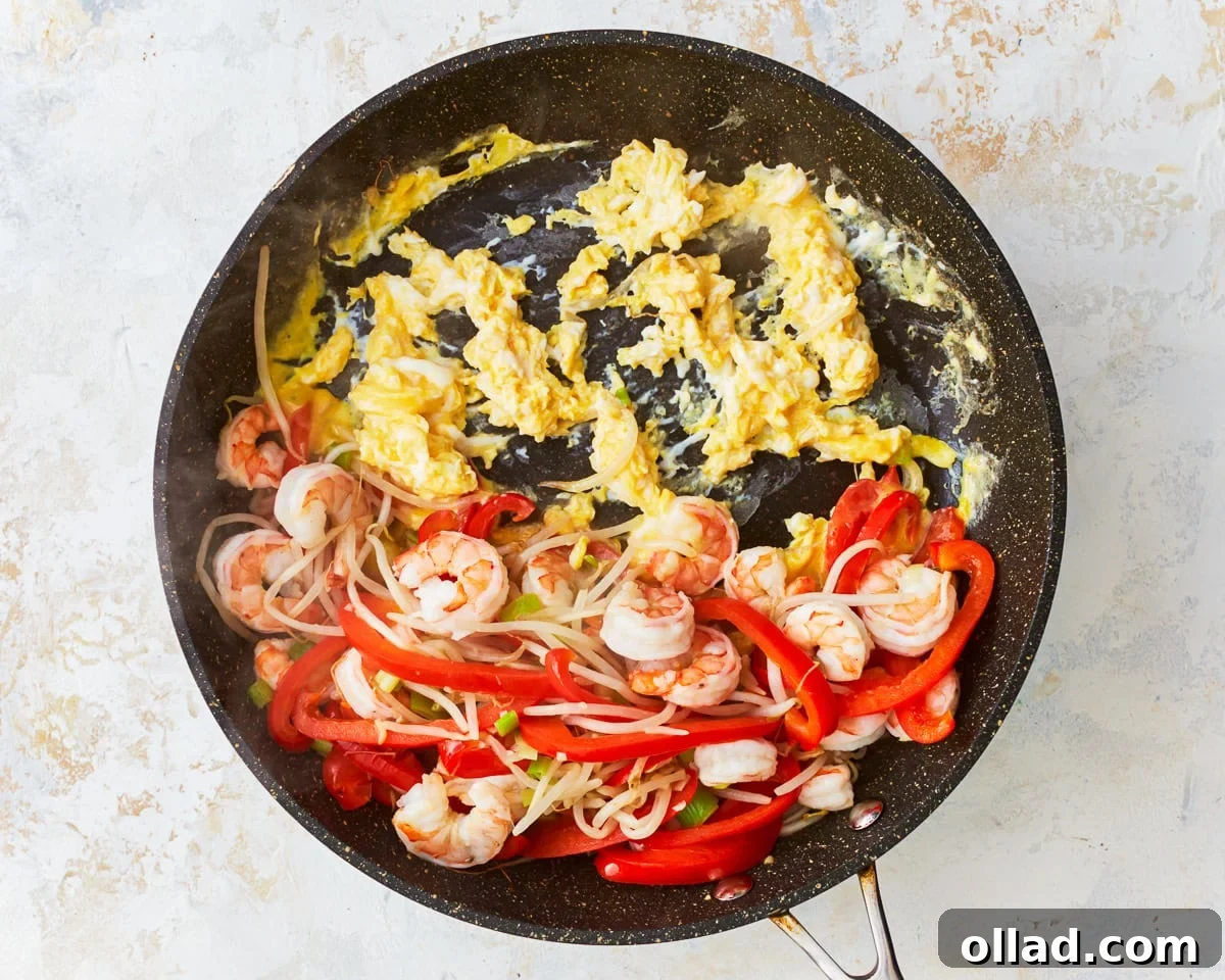Eggs cooking in skillet with vegetables and shrimp for gluten-free pad thai