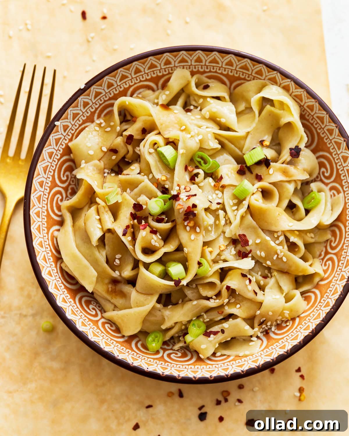 Gluten-free egg noodles in a bowl with vibrant green onions, crunchy sesame seeds, and a sprinkle of fiery red pepper flakes, ready to be enjoyed.