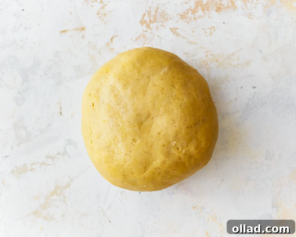 A smooth and elastic ball of gluten-free egg noodle dough resting on a lightly floured surface after kneading.