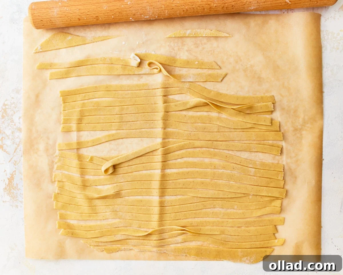 Gluten-free egg noodle dough precisely cut into even strips on parchment paper, ready for cooking.