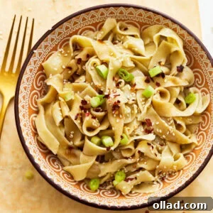 Gluten-free egg noodles in a bowl with green onions, sesame seeds, and red pepper flakes