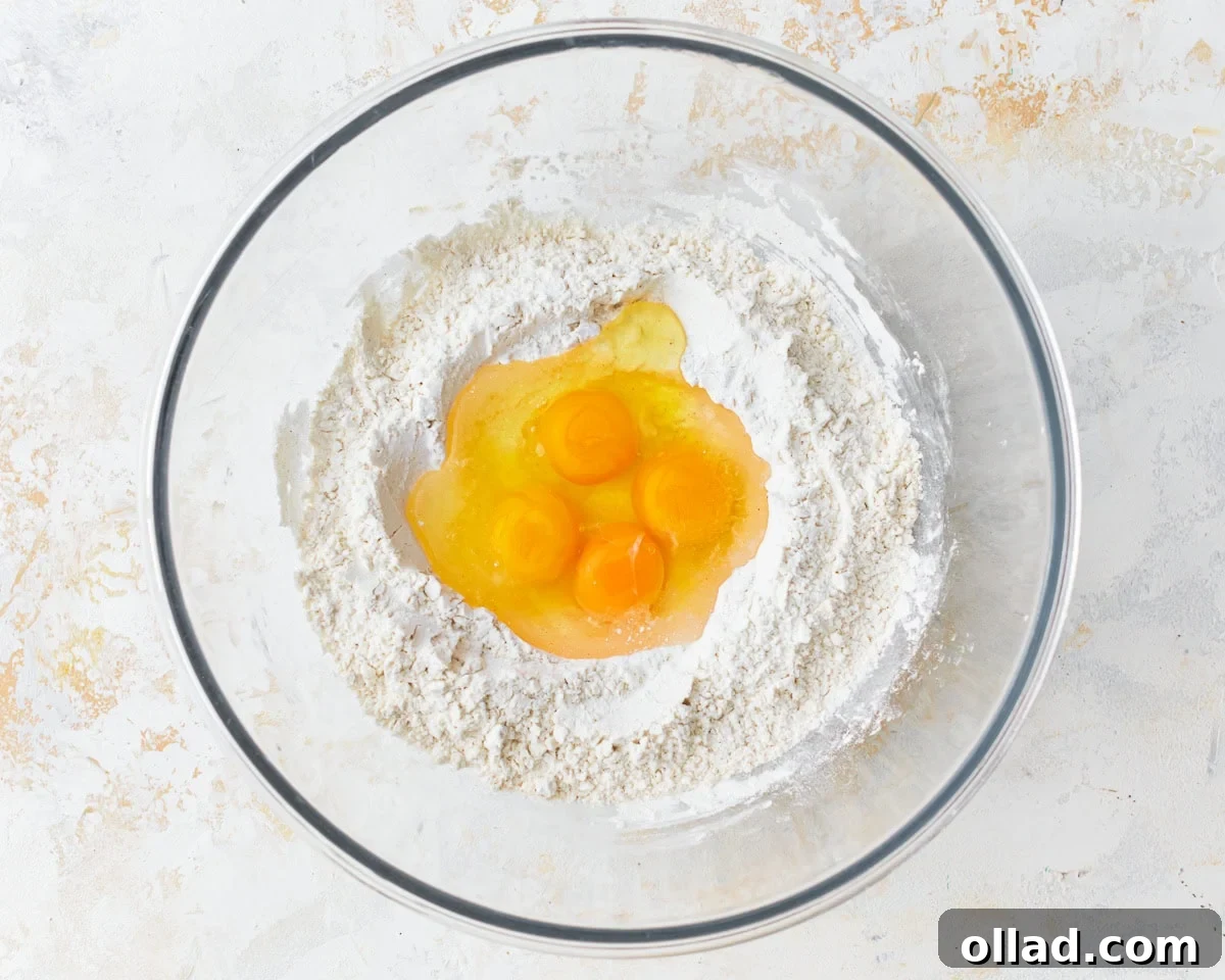 Fresh eggs cracked into a well formed in the center of the dry gluten-free noodle ingredients in a glass mixing bowl.
