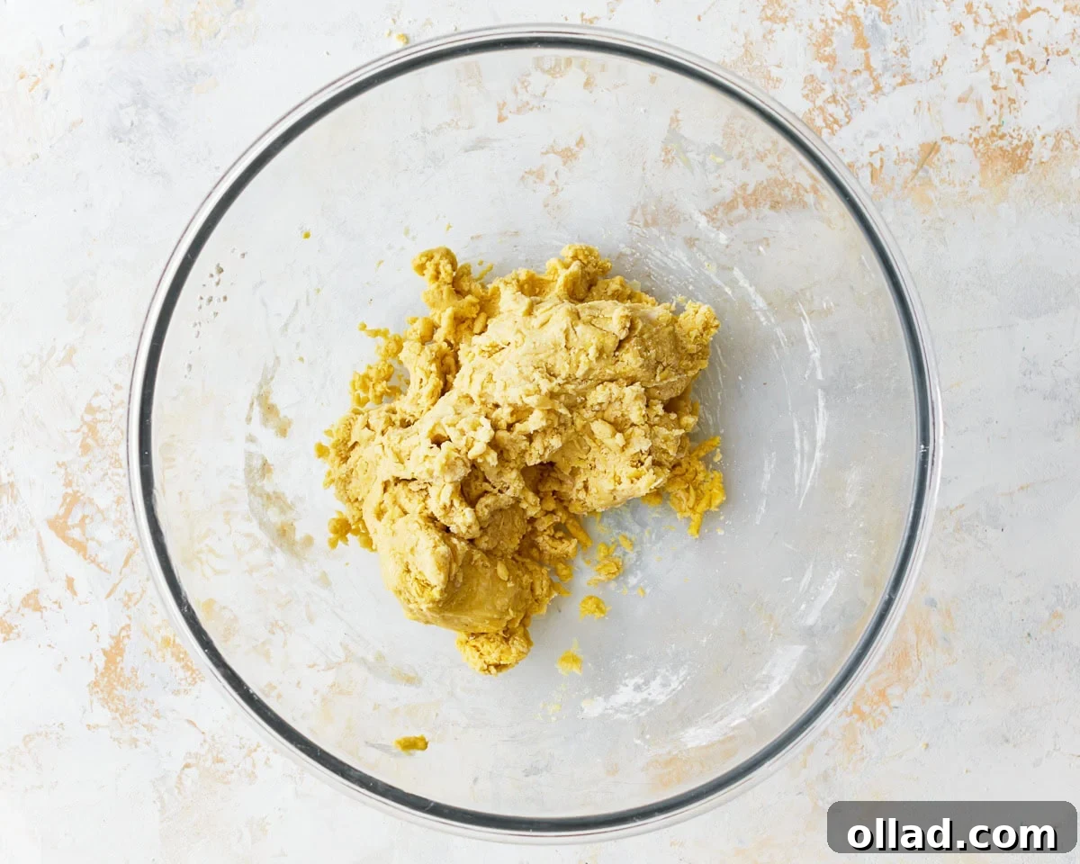 The initial shaggy dough for gluten-free egg noodles forming in a glass mixing bowl, with dry and wet ingredients just starting to combine.