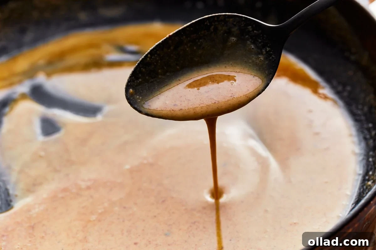A spoon scooping gluten-free roux from a skillet.