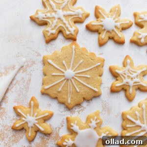 Decorated gluten-free sugar cookies shaped like snowflakes, with white icing on a light textured background.
