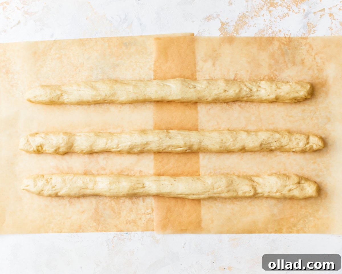 Gluten-free challah bread dough divided into three and rolled into a long rope shape on parchment paper.