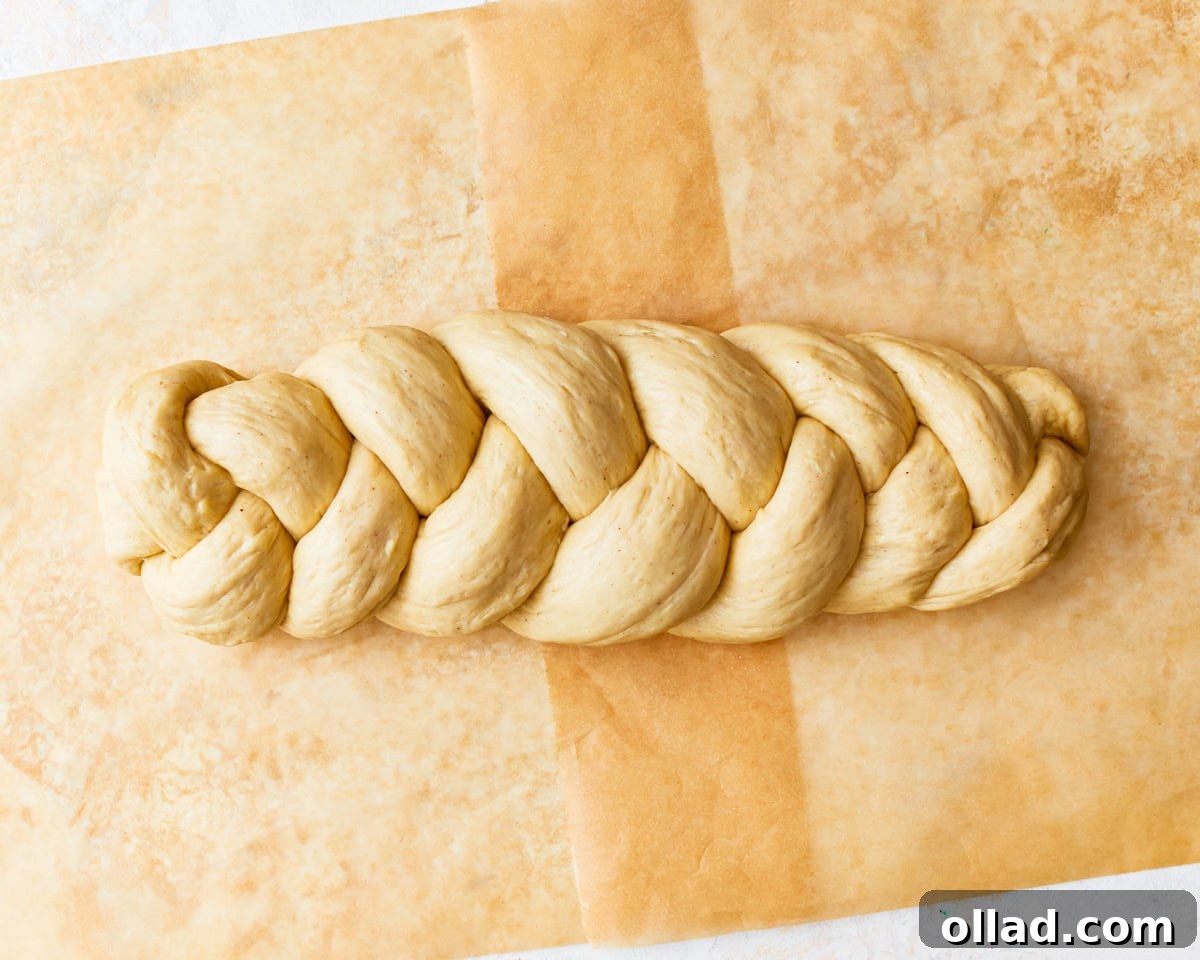 Gluten-free challah bread dough shaped into a braided loaf on a piece of parchment paper.