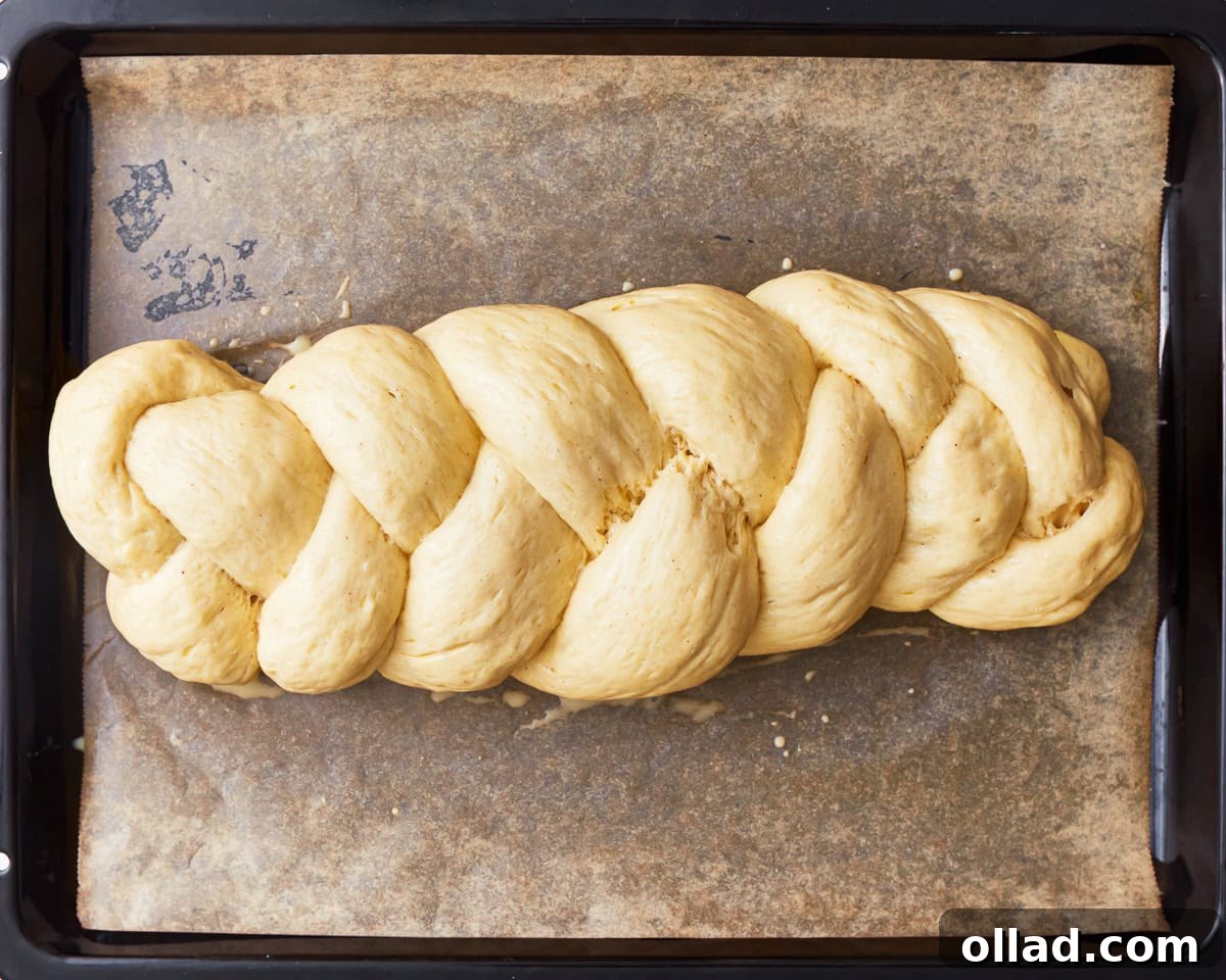Gluten-free challah bread dough shaped into a braided loaf on a parchment lined baking sheet.