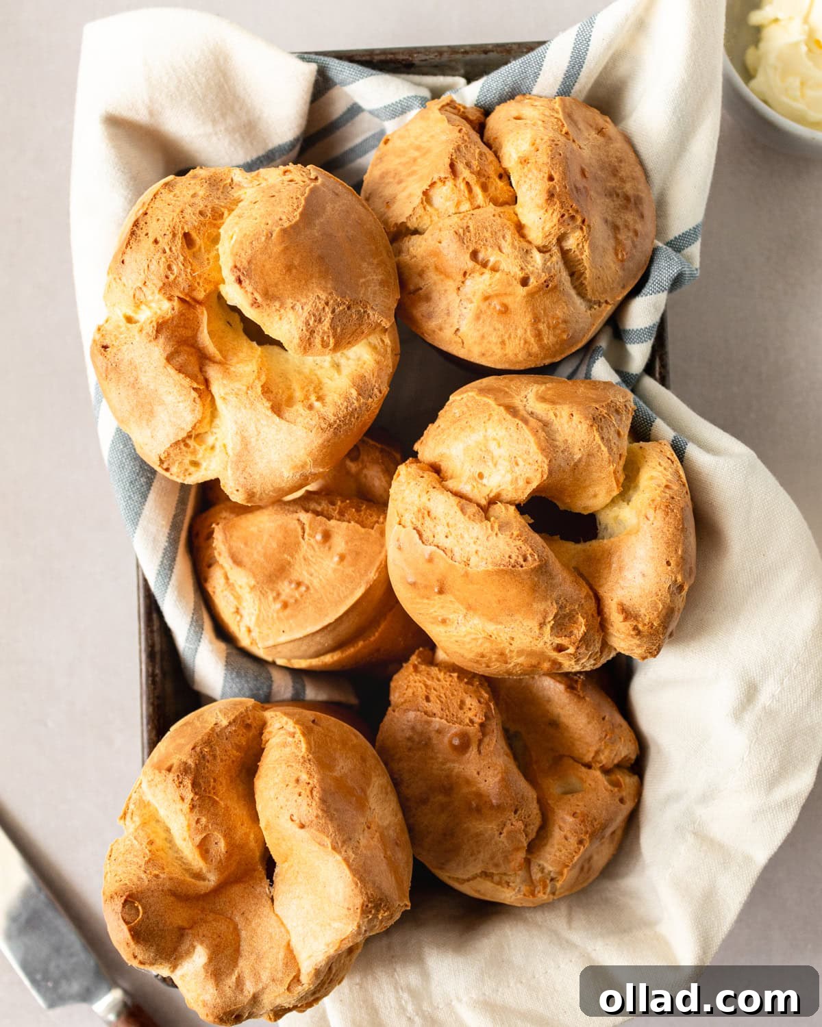 Overhead view of golden-brown popovers resting in a towel-lined baking pan, ready to be served.