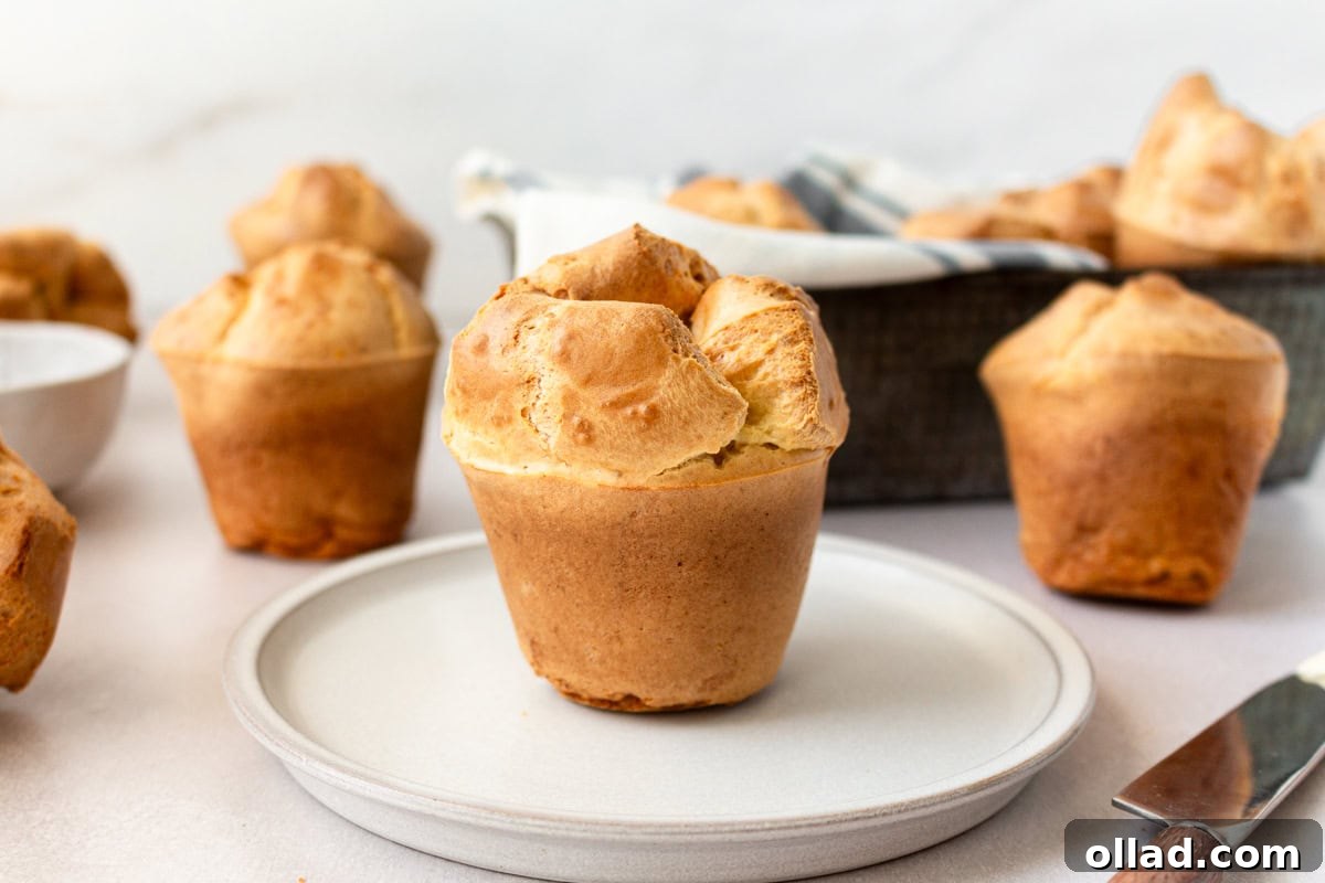 A single gluten-free popover standing tall on a white plate, showcasing its golden crust and airy texture.