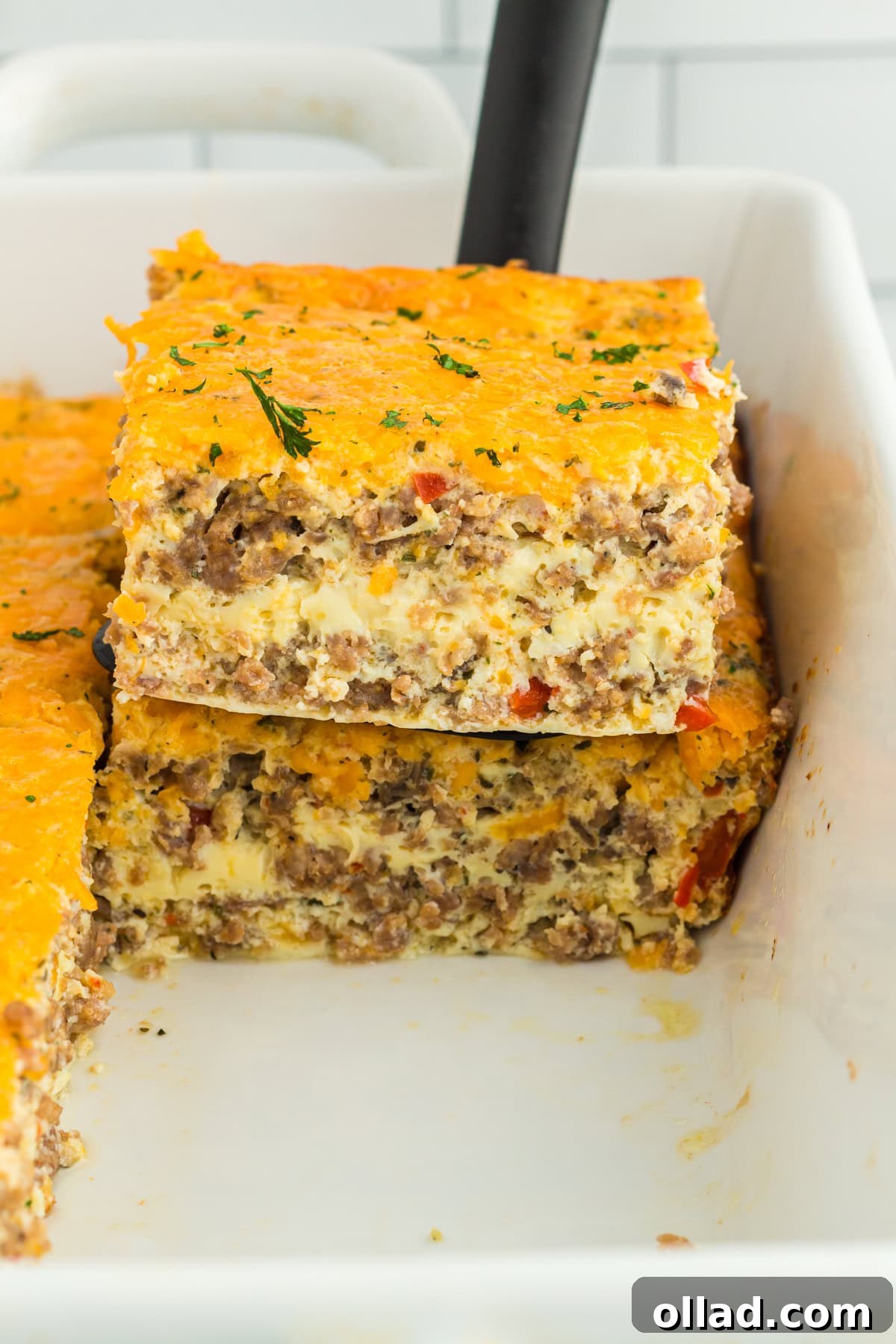 spatula take piece of sausage casserole out of white baking pan
