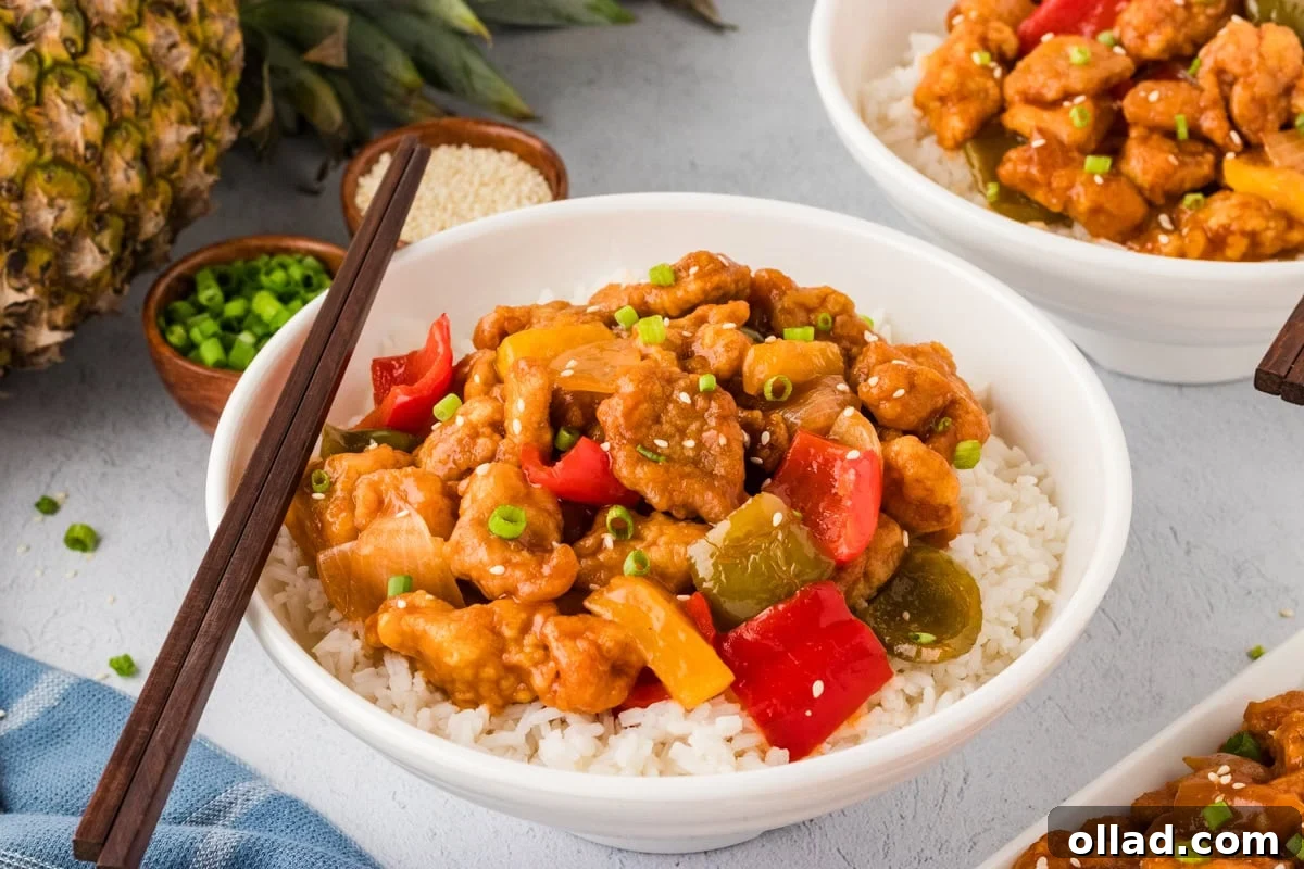 Irresistible Gluten-Free Sweet and Sour Chicken 7 closeup side view of sweet and sour chicken over rice in white bowl with wooden chopsticks