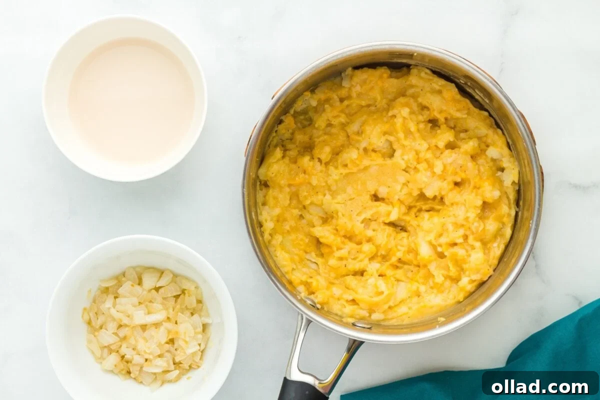 Delectable Gluten-Free Pierogi 13 A large pot filled with creamy mashed cheesy potatoes, positioned next to a white bowl containing milk and another white bowl holding sauteed onions, all ready for combination.