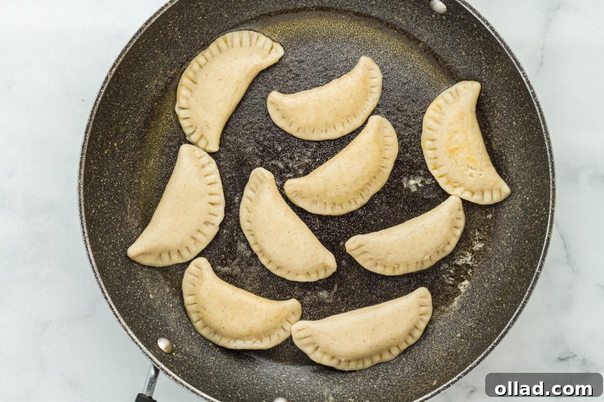 Delectable Gluten-Free Pierogi 21 Nine boiled pierogi starting to brown in a black frying pan, indicating the transition from boiling to pan-frying for a crispy finish.