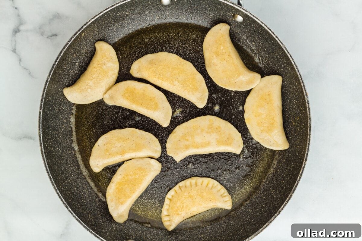 Perfectly browned pierogi sizzling in a black frying pan, showcasing their crispy, golden exterior.