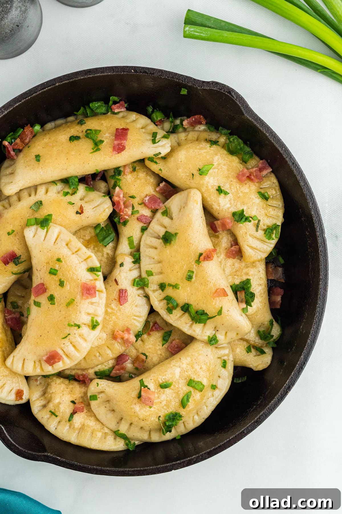 Delectable Gluten-Free Pierogi 4 Overhead view of crispy, pan-fried gluten-free pierogi in a cast iron skillet, topped with bacon bits and fresh scallions.