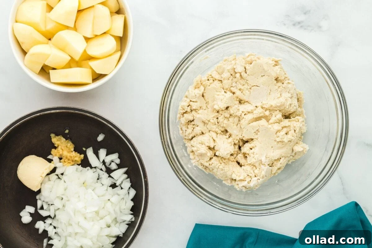 Delectable Gluten-Free Pierogi 8 Overhead view showing pierogi dough forming in a glass bowl, with separate bowls of chopped onions and cubed potatoes on a white background.