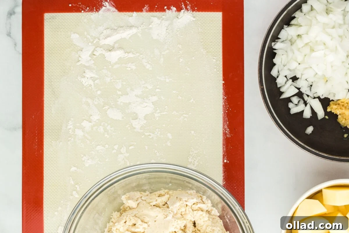 A glass bowl containing smooth pierogi dough rests on a lightly floured silicone mat, illustrating the ideal dough consistency.