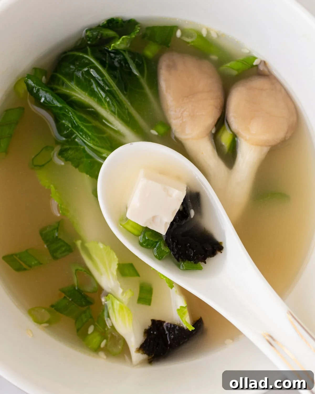 Savory Gluten-Free Miso Bowl 4 white soup spoon with a piece of tofu and seaweed hovering over bowl of gluten-free miso soup