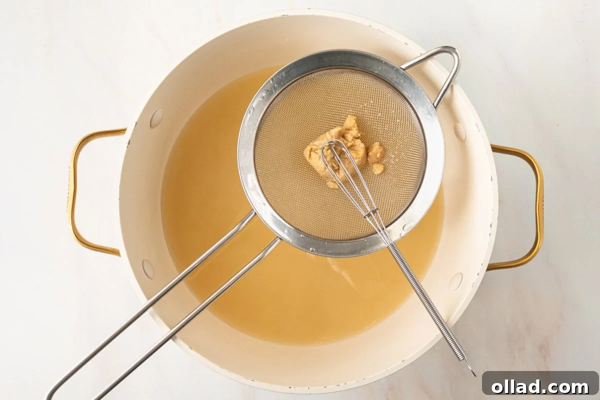 Savory Gluten-Free Miso Bowl 9 a small sieve with white miso paste being whisked into gluten-free miso soup in a large pot