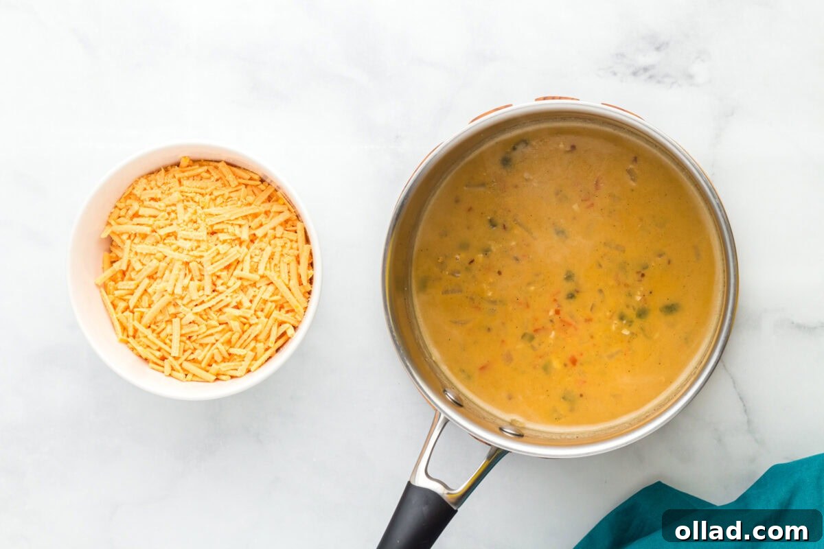 Shredded vegan cheese slowly melting and blending into the simmering queso mixture within a stainless steel pot, creating a creamy texture.