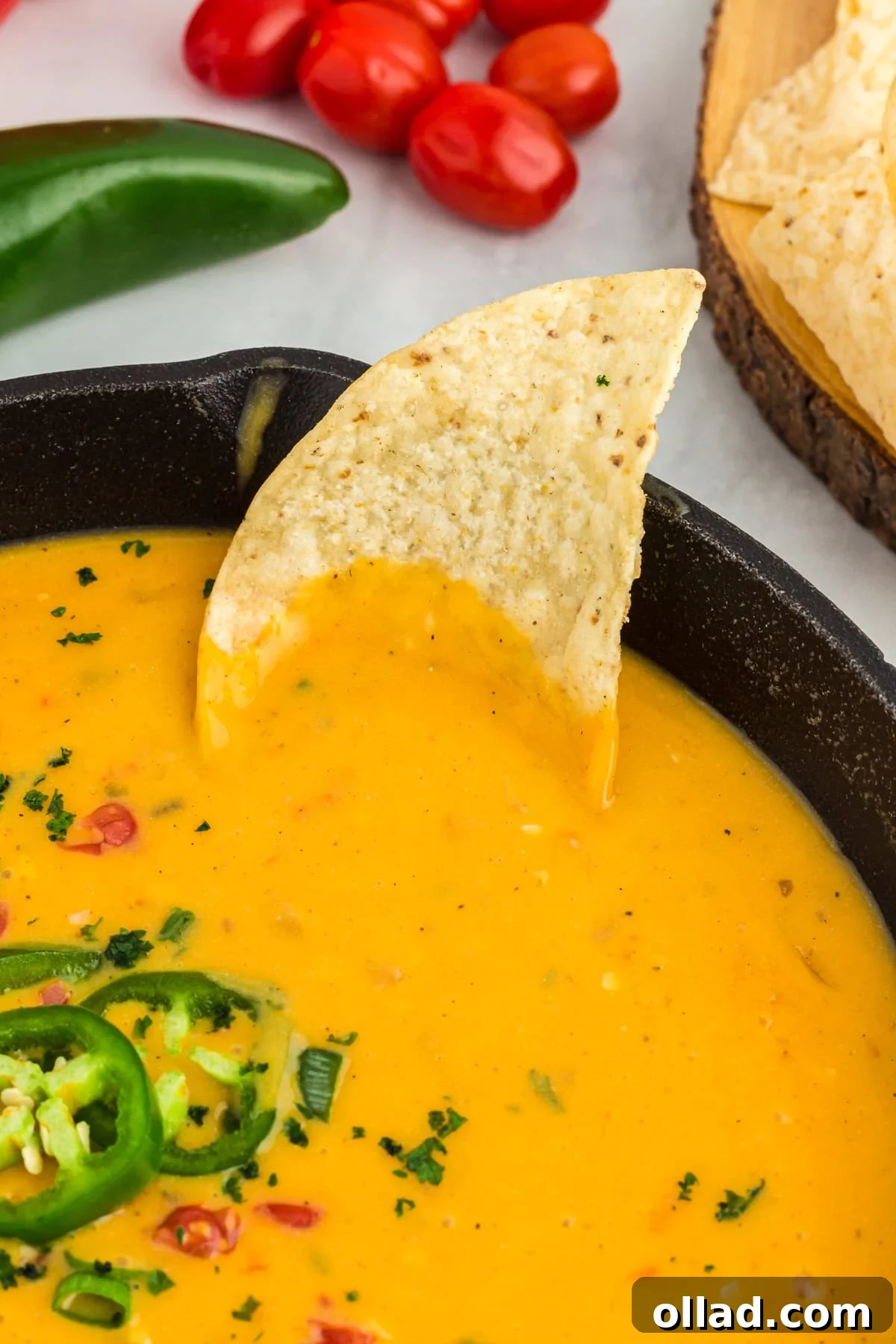 A crisp tortilla chip is dipped into the smooth, creamy vegan queso inside a black skillet, highlighting its rich texture and inviting presentation.