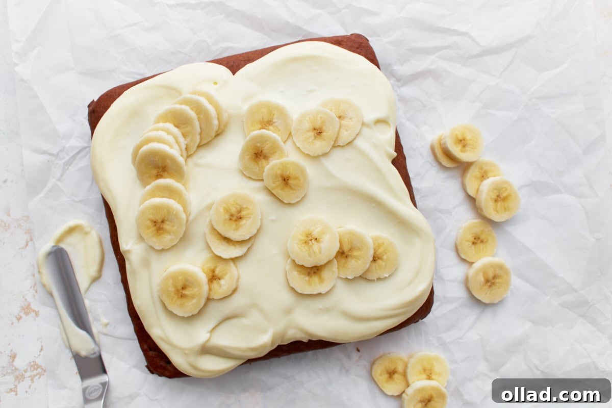 Irresistible Gluten-Free Banana Cake 11 Gluten-free banana cake topped with cream cheese frosting and fresh banana slices on white parchment paper