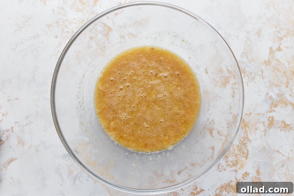 Irresistible Gluten-Free Banana Cake 5 mashed bananas, sugar, and egg mixture in glass mixing bowl on a light surface