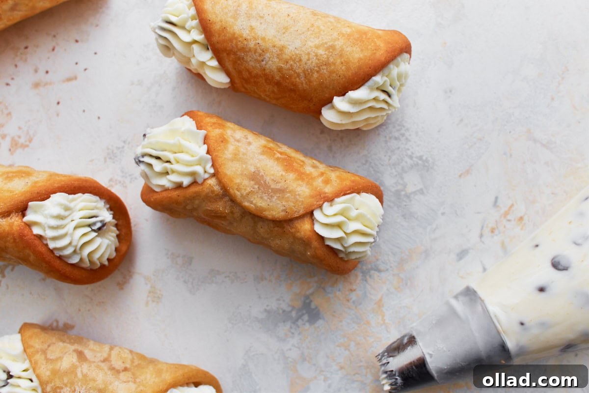 Close-up of gluten-free cannoli shells filled with ricotta cream, garnished with piped cream at both ends, resting on a light textured surface