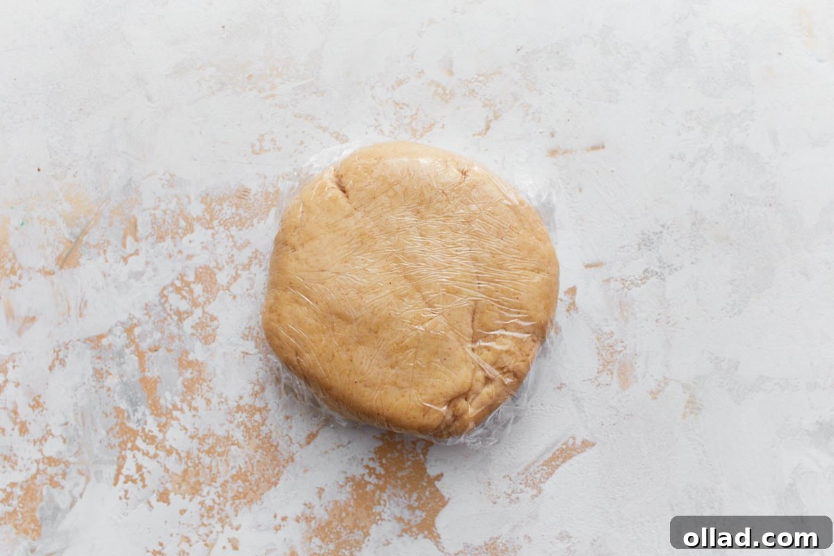 A ball of smooth gluten-free cannoli dough resting in the center of a clear glass mixing bowl, placed on a light-colored, textured surface lightly dusted with flour