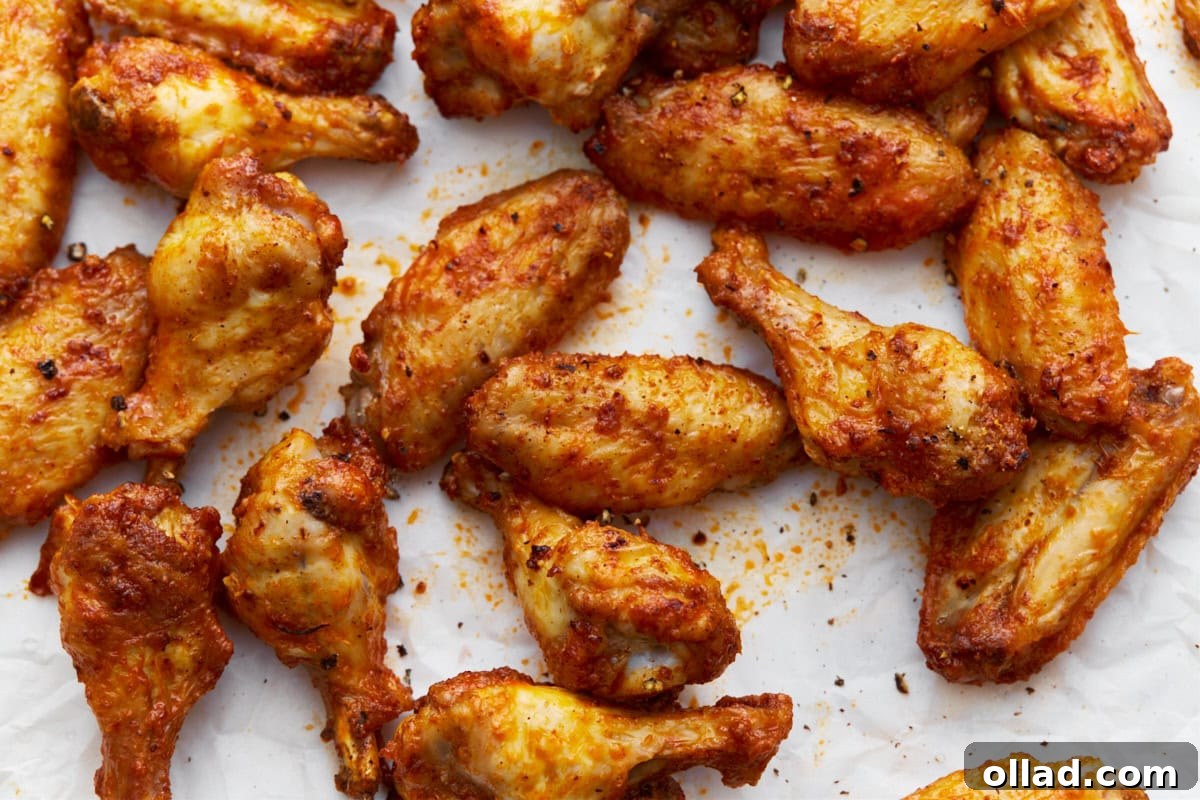 Overhead view of a tray of crispy, golden-brown gluten-free chicken wings seasoned with spices and arranged on parchment paper, showing their lightly charred edges and flavorful coating