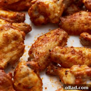 closeup of a tray of crispy, golden-brown gluten-free chicken wings seasoned with spices and arranged on parchment paper, showing their lightly charred edges and flavorful coating