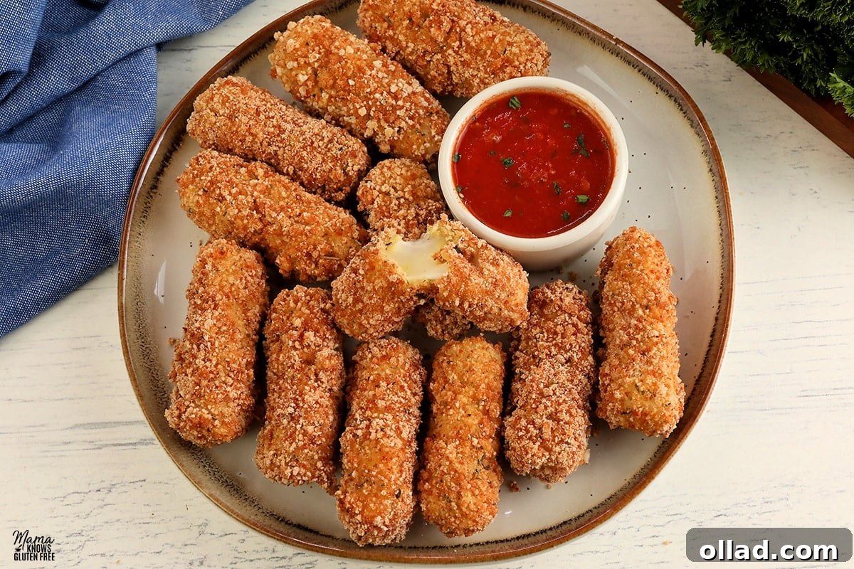 Gluten-Free Game Day Victory Bites 3 gluten-free mozzarella sticks on a white plate with one broken open to see the melted cheese
