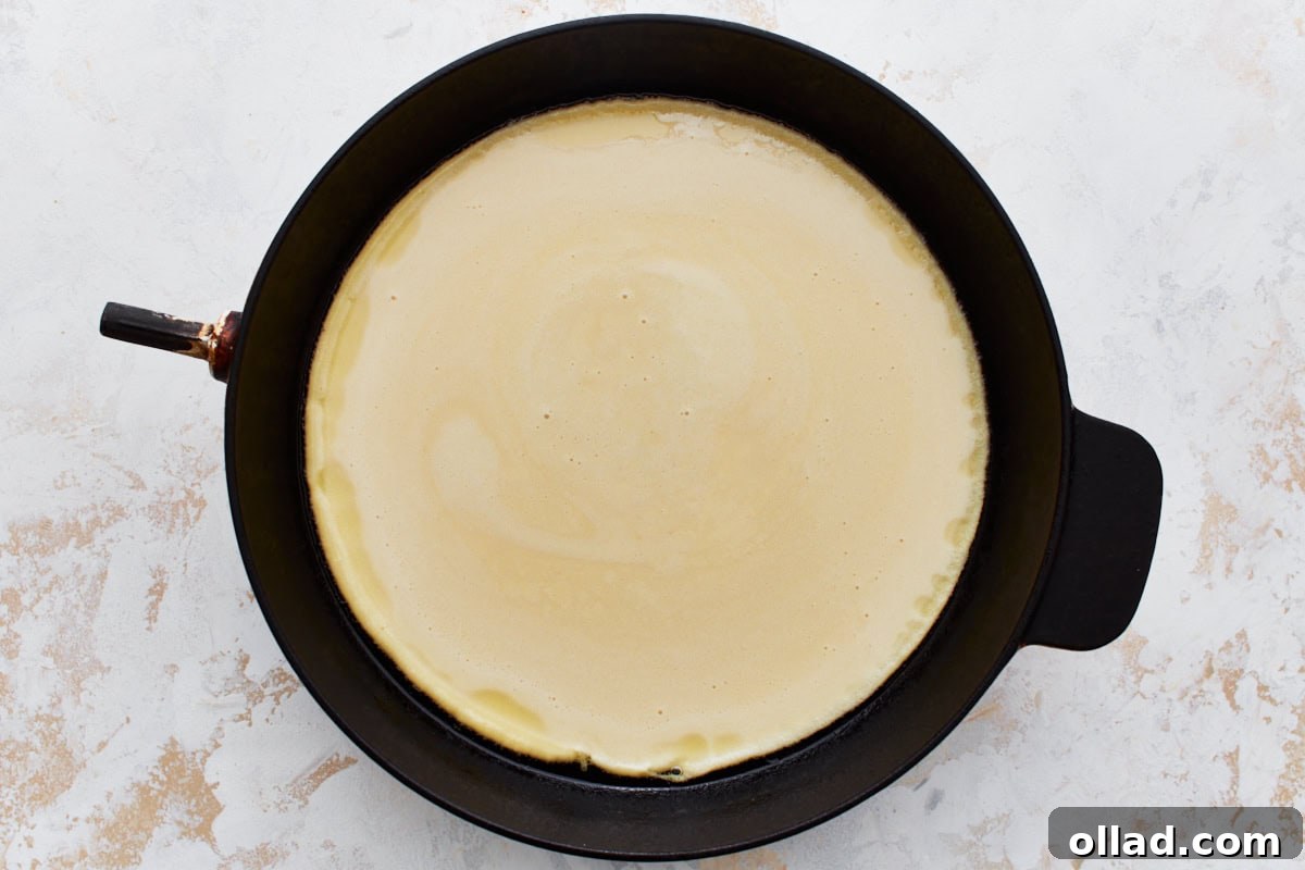 A cast iron skillet, lightly coated with olive oil, holding the uncooked chickpea flour batter before baking.