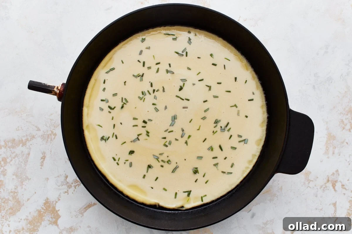 Uncooked chickpea batter in a cast iron skillet, sprinkled generously with freshly chopped rosemary, ready for the oven.