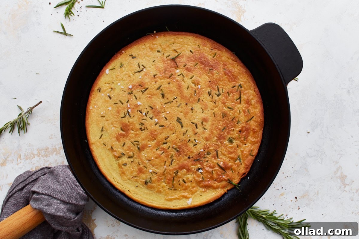 Freshly baked farinata, golden brown and perfectly crispy around the edges, still in its cast iron skillet, garnished with rosemary and flaky salt.