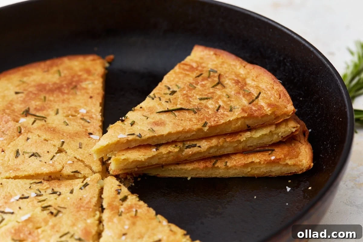 A side profile of multiple slices of farinata stacked in a cast iron skillet, revealing its enticing golden crust and soft interior. Garnished with fresh rosemary and a sprinkle of sea salt.