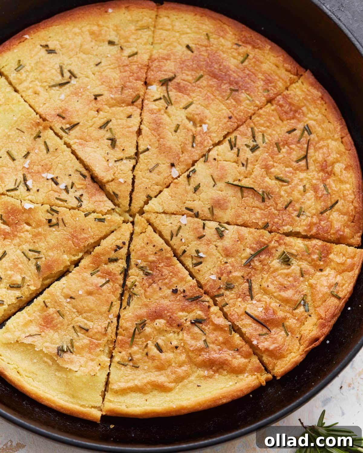 A top-down view of a whole Farinata in a cast iron skillet, already sliced into wedges and beautifully garnished with fresh rosemary sprigs and a dusting of flaky salt.