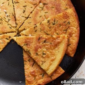A sliced farinata (chickpea flatbread) in a cast iron skillet, garnished with rosemary and flaky salt.