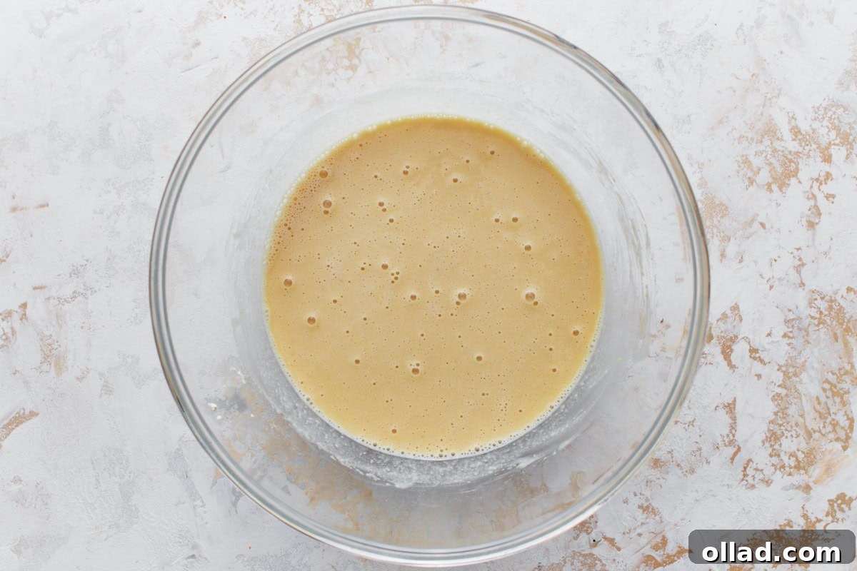 A glass bowl containing the mixed chickpea batter, now smooth and infused with olive oil, ready for resting.