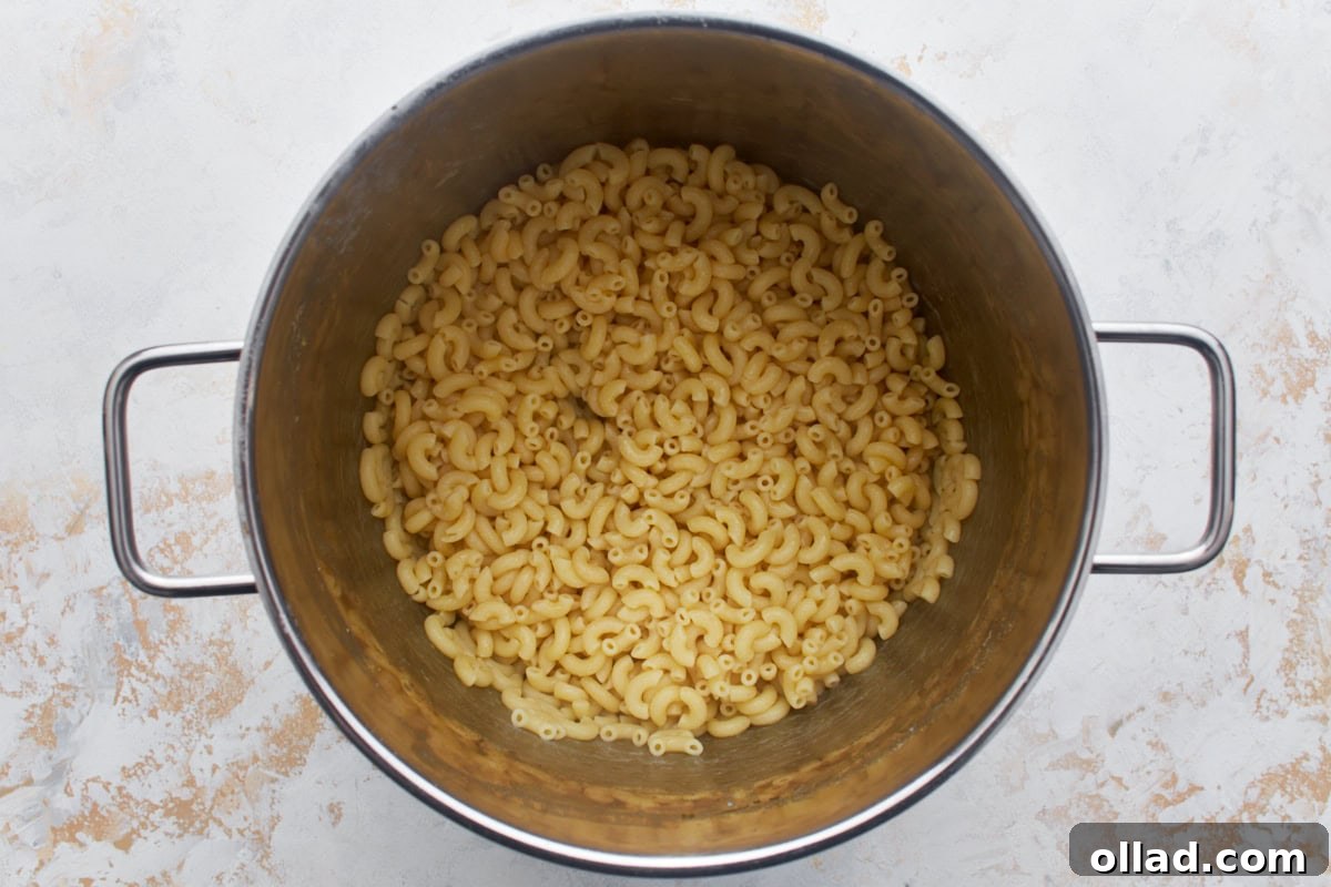 Gluten-free macaroni in a large pot coated with melted butter, ready for the next step.