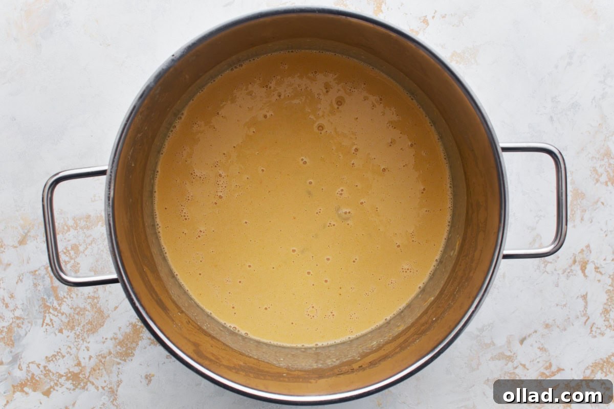 Gluten-free macaroni in a large pot covered in an egg and milk mixture, ready for the cheese.
