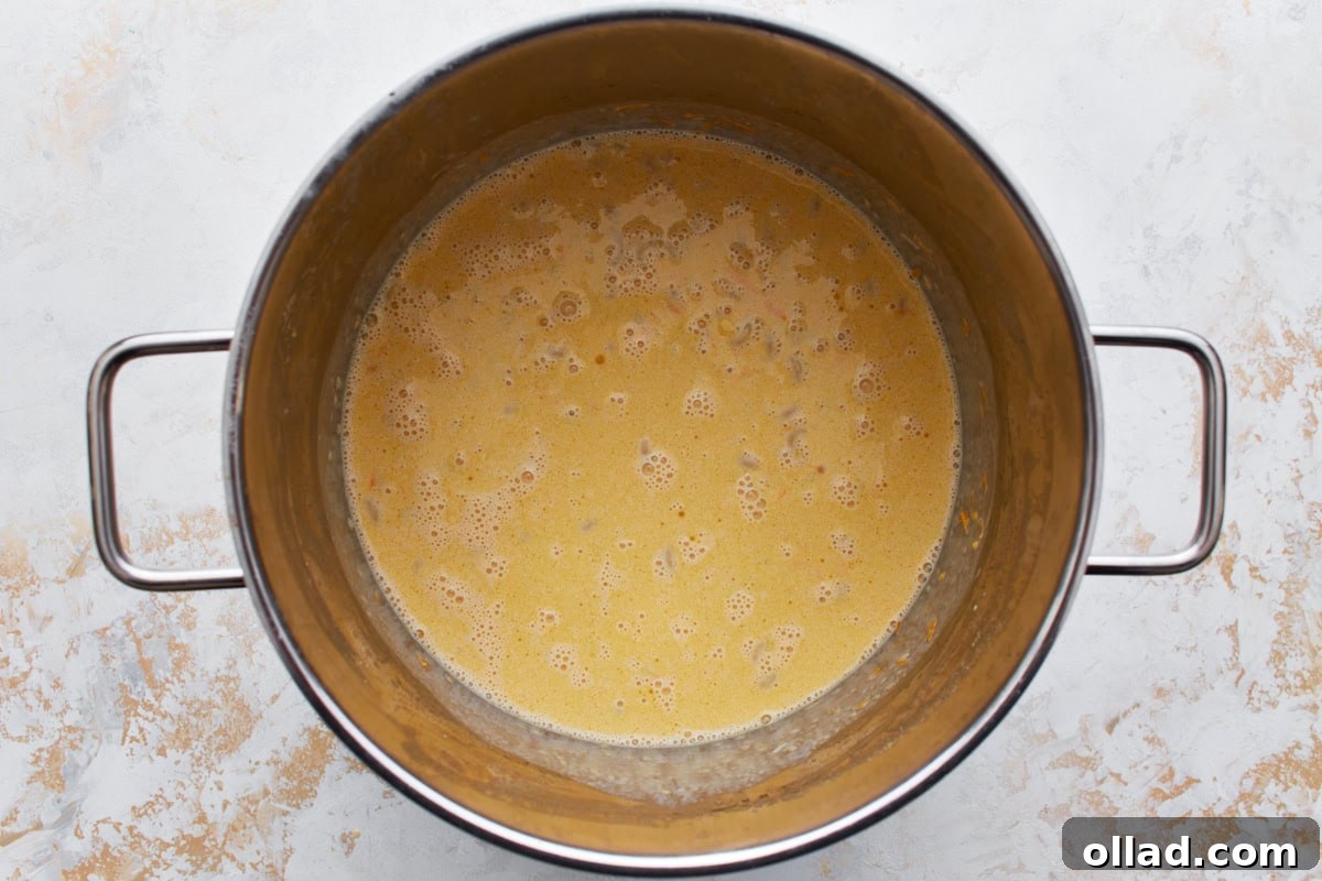 Gluten-free macaroni in a large pot covered in an egg and milk mixture that's simmering gently on the stove.