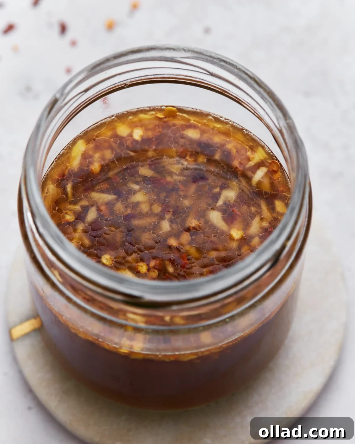A top-down view of gluten-free stir-fry sauce in a jar, showcasing its rich brown color with garlic and red chili flakes floating on the surface.