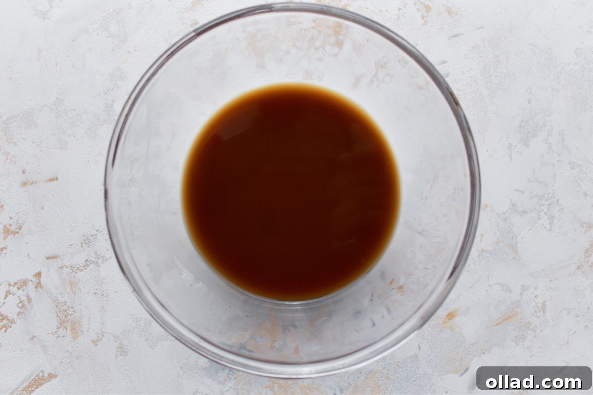 A clear mixing bowl containing a smooth, glossy brown gluten-free stir-fry sauce, ready for use.