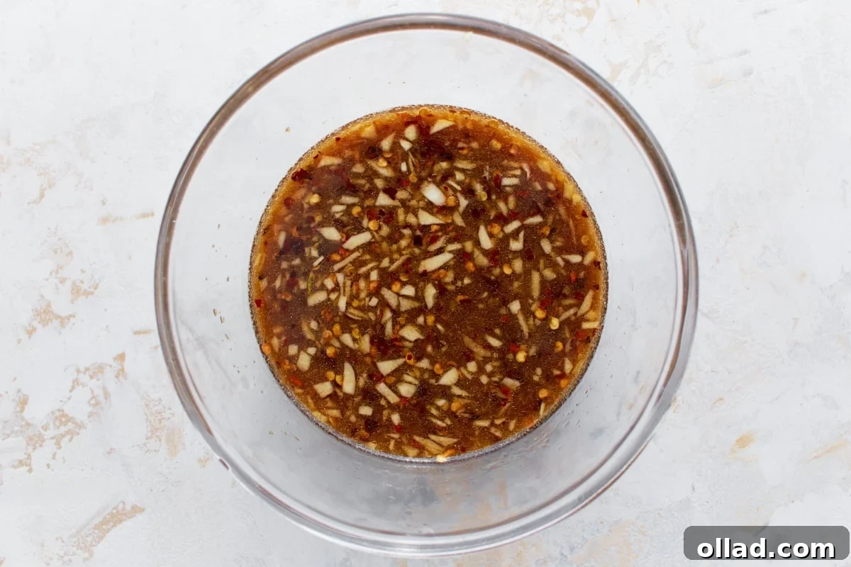 A clear mixing bowl of gluten-free stir-fry sauce, showing finely chopped garlic, red chili flakes, and a rich texture that enhances its appearance.